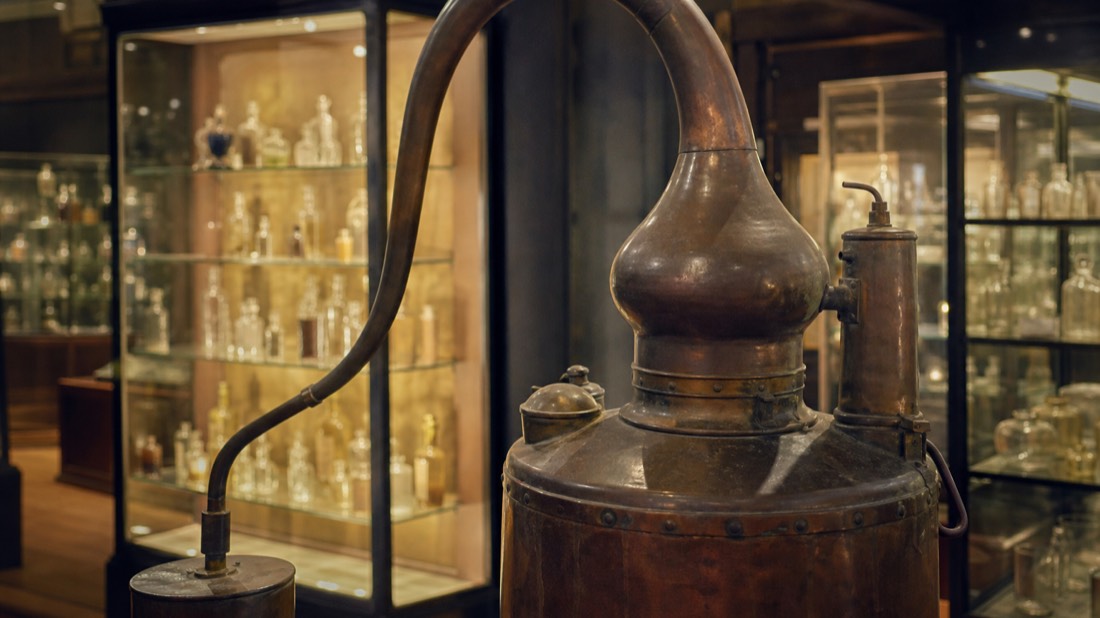 Antique copper distillation still in a Paris perfume museum beside vitrines of flacons