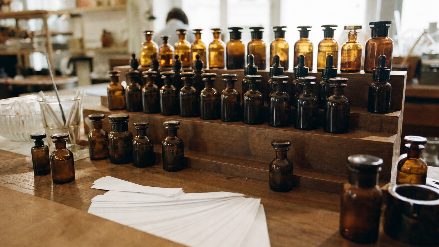 Rows of amber essence bottles and fanned paper scent strips on a wooden perfume workshop bench in Paris