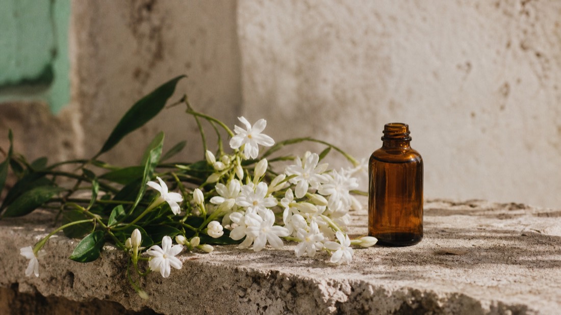 Fresh jasmine flowers beside an amber essence bottle on a weathered stone ledge in the south of France